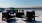The Charley Apartments | A modern rooftop patio at Charley Apartments in Allston MA features four black cushioned chairs around a round table, with potted plants and blue sky in the background. | Apartments with Balcony in Boston 