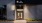 The Charley Apartments | The entrance to The Charley Apartments in Allston MA features a modern design with the sign The Charley above glass doors, the number 46 on the wall, plants along the walkway, and exterior lights illuminating the area at dusk. | B