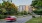 The Charley Apartments | Cars drive along a curved road lined with trees and grass, The Charley Apartments in Allston MA rise in the background on a sunny day. | Apartments with Washer & Dryer in Boston 