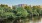 The Charley Apartments | A person rows a red single scull boat on a calm river, surrounded by green trees with The Charley Apartments in Allston MA visible in the background under a clear blue sky. | Wheelchair accessible Apartments in Boston 