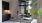 The Charley Apartments | Modern dining nook at The Charley Apartments in Allston MA features a round white table, three black stools, a vase of flowers, and books. A large window overlooks the patio while dark cabinets and soft lighting create a cozy atmo